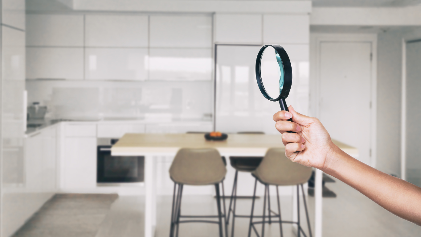 Hand holding magnifying glass in modern kitchen for mold inspections.