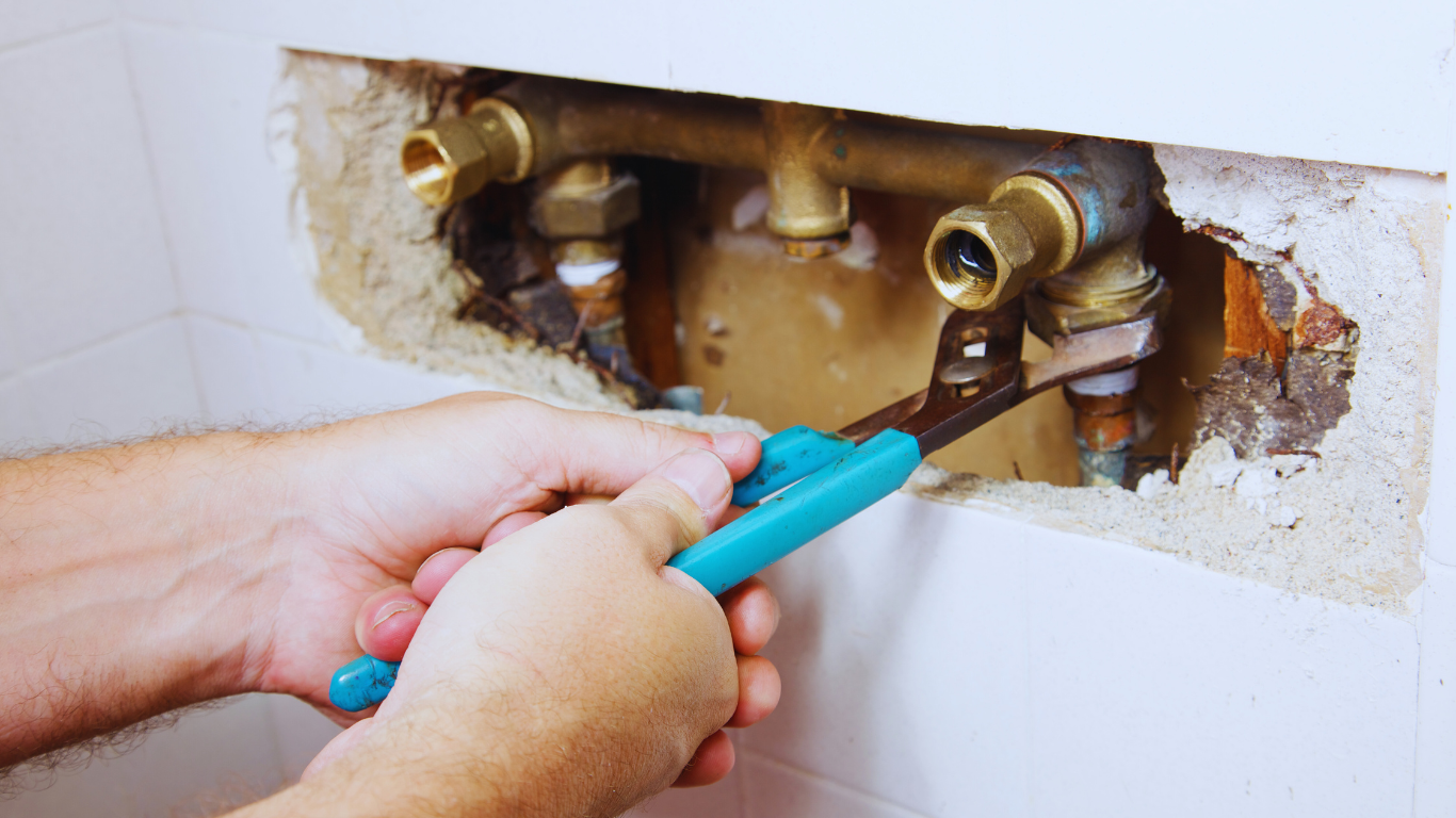 Person fixing a water leak behind the wall, showcasing water leak detection and plumbing repair services.